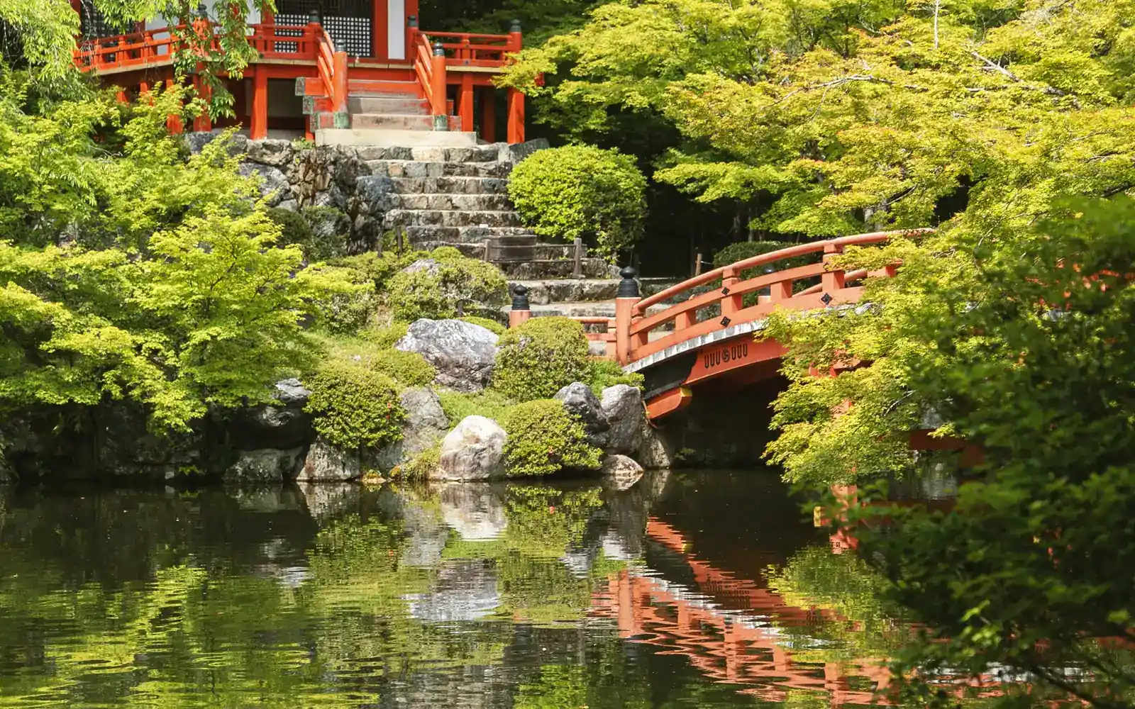 A red bridge over a still garden pond