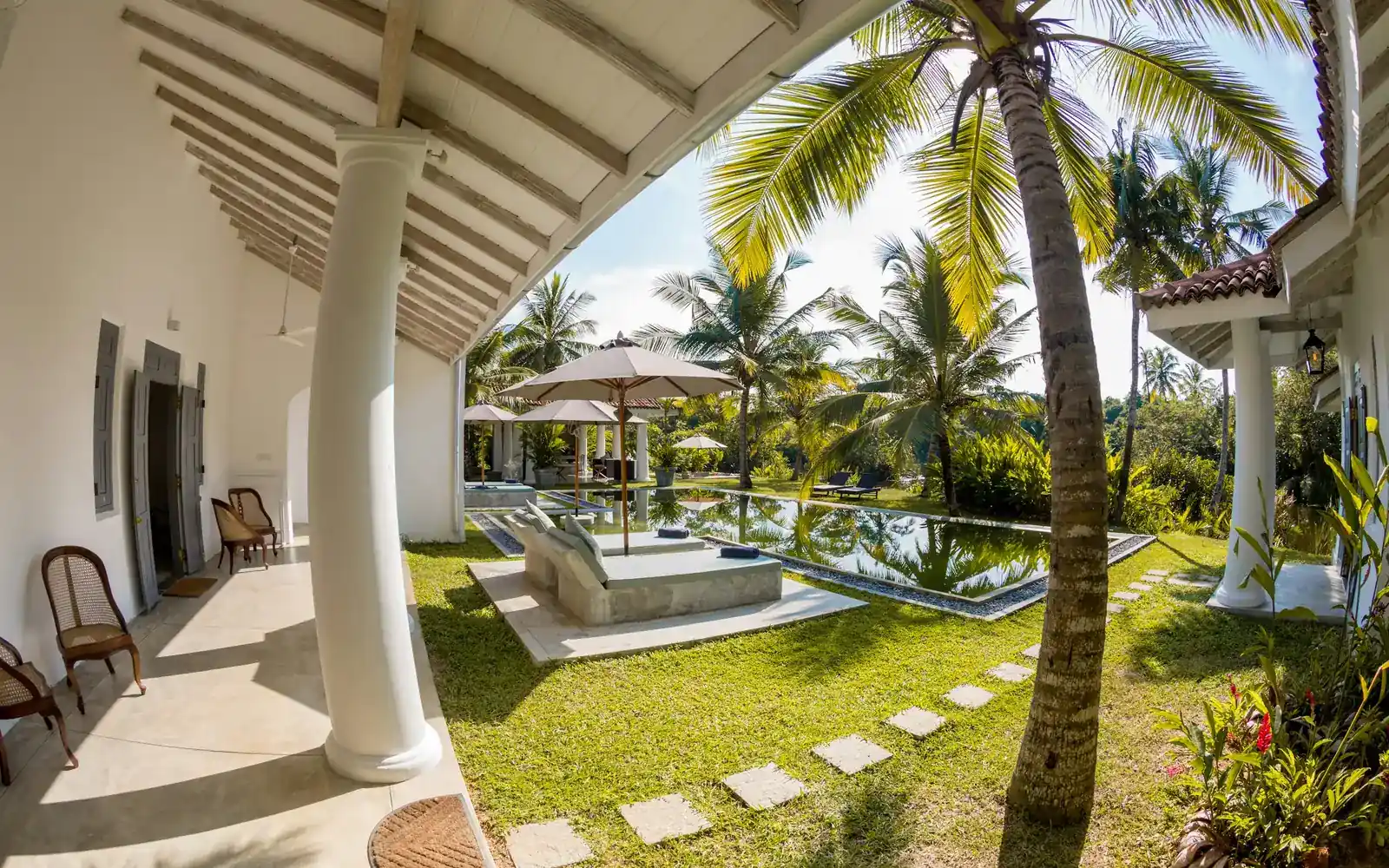 A villa veranda overlooking a palm garden and pool