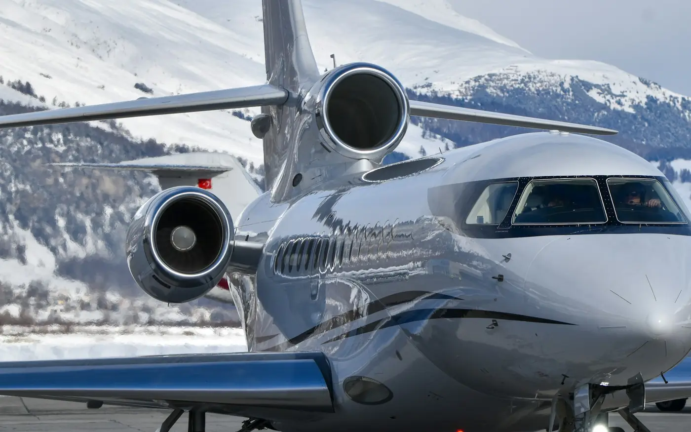 A silver private jet taxiing below snow-covered mountains